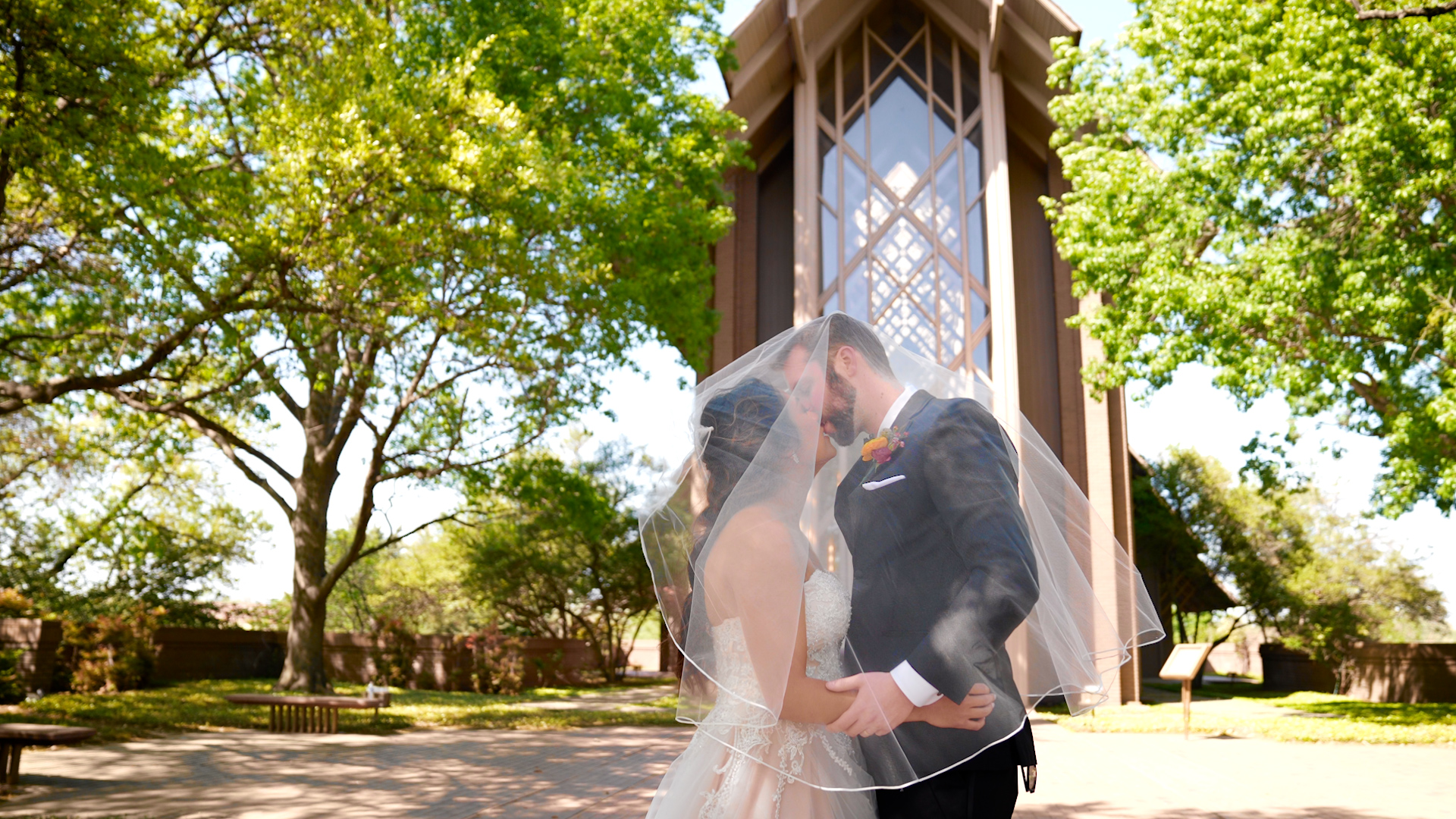 Bride and Groom are covered under her veil, going for a deep kiss in front of the beautiful Marty Leonard Chapel 