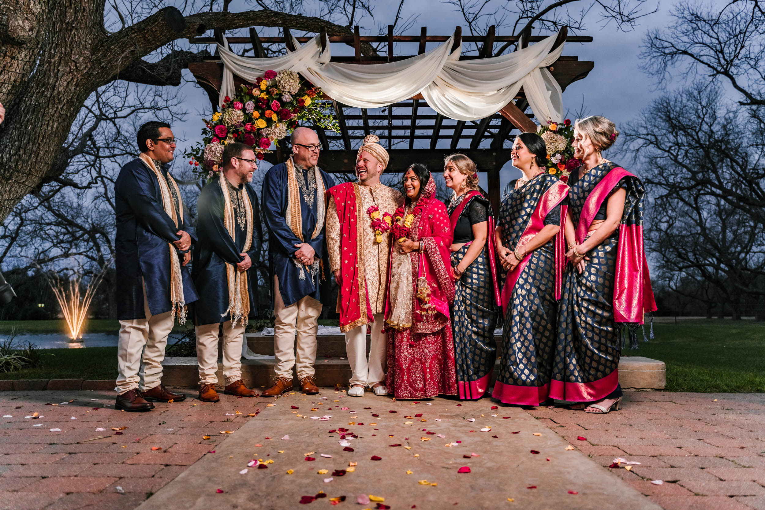 A Caucasian groom and Indian bride posing with their bridal party, all wearing their traditional outfits at The Orchard Event Venue & Retreat - Wedding Venue