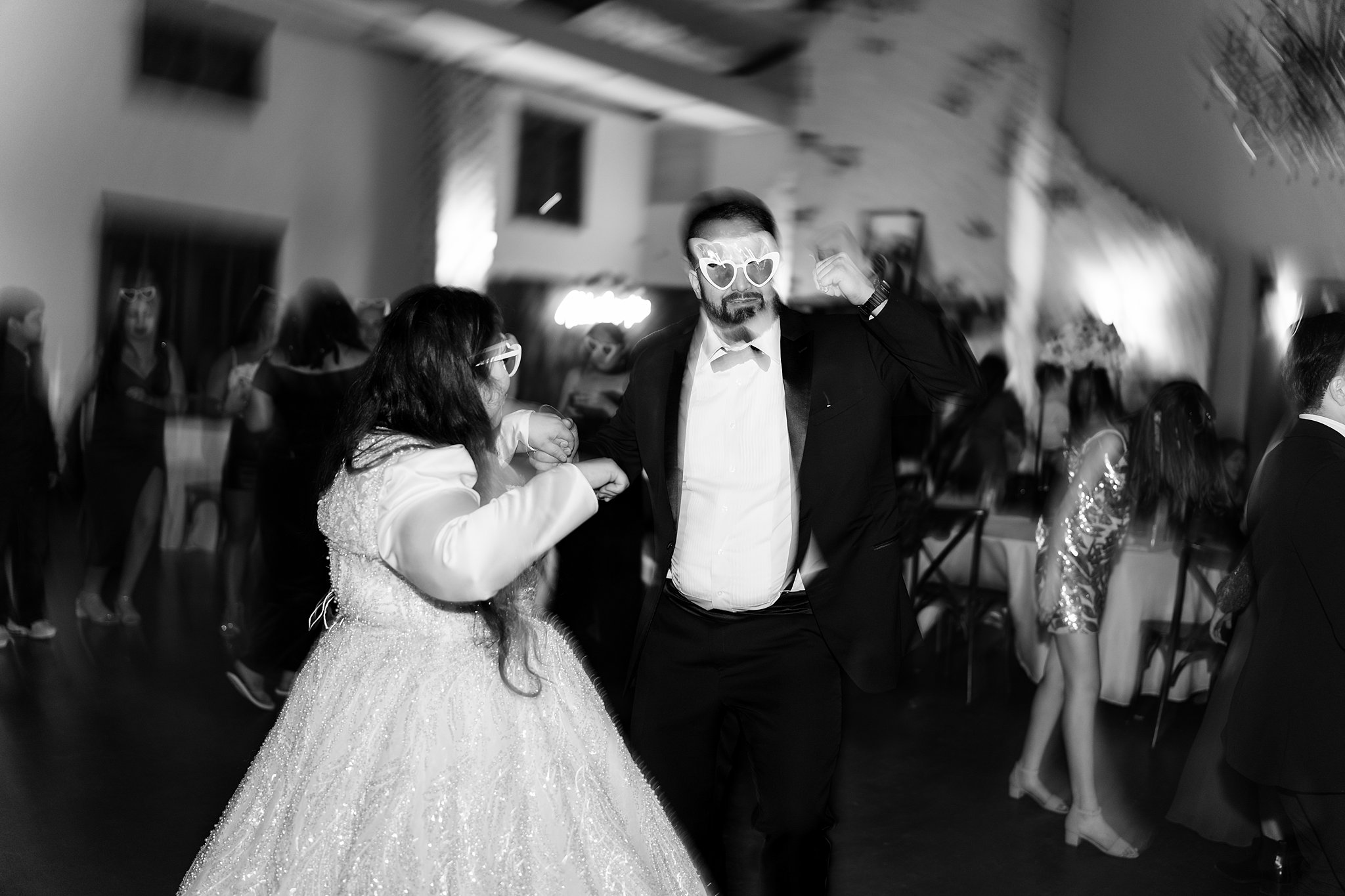 A bride and groom dance on the dance floor in silly sunglasses