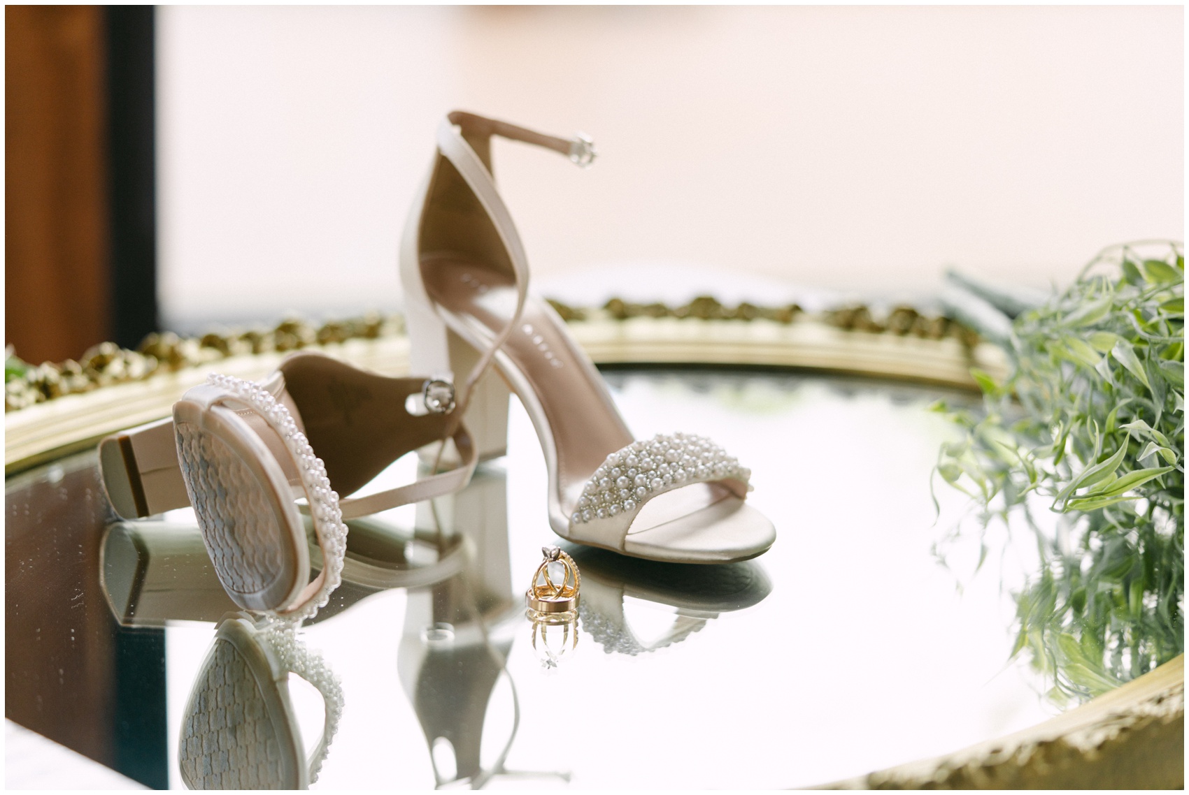 Details of a bride's wedding shoes and rings on a mirror table