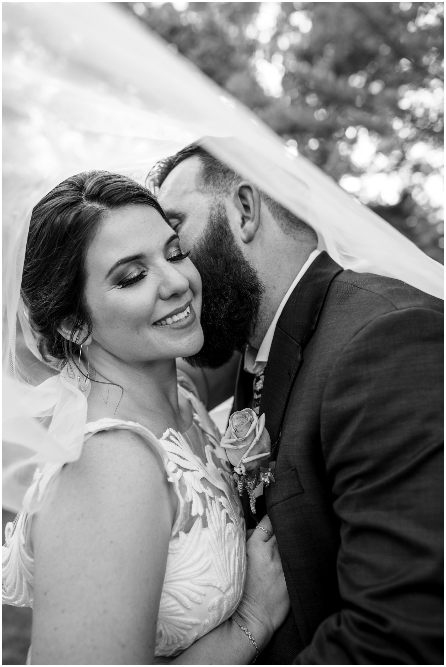 A bride smiles while her groom kisses her cheek during their D'Vine Grace Vineyard wedding