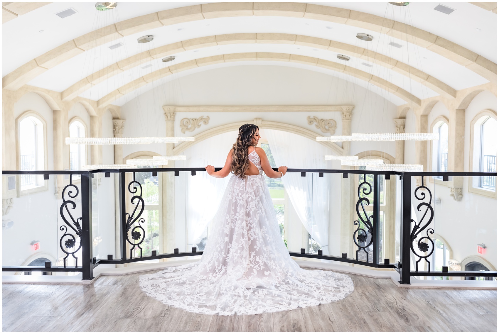 A bride stands on a balcony railing showing her long lace dress while smiling over her shoulder at her Knotting Hill Place Wedding