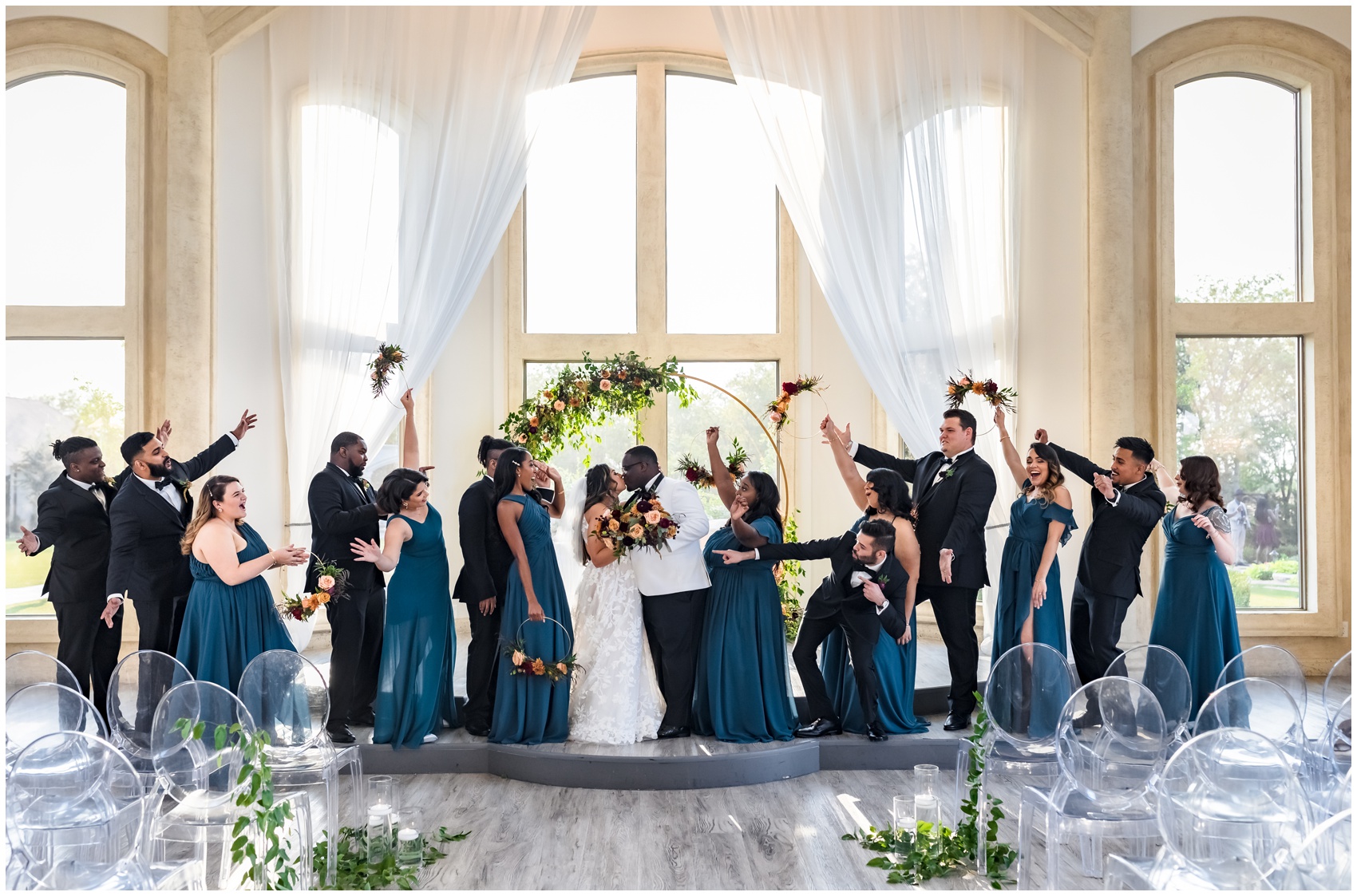 Newlyweds kiss while their wedding part throws their hands up and celebrates on the altar during their Knotting Hill Place Wedding