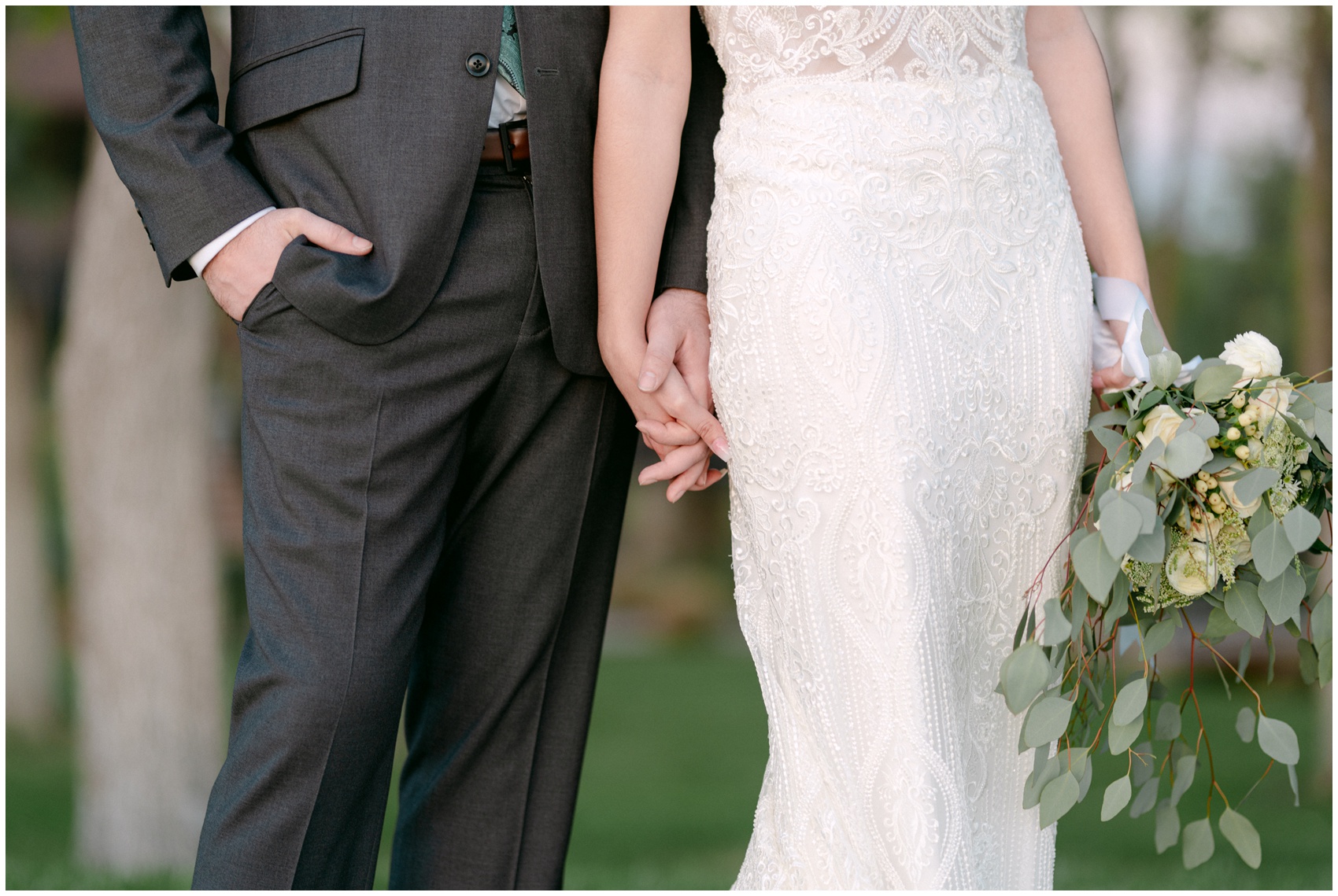 Newlyweds hold hands in a lace dress and grey suit