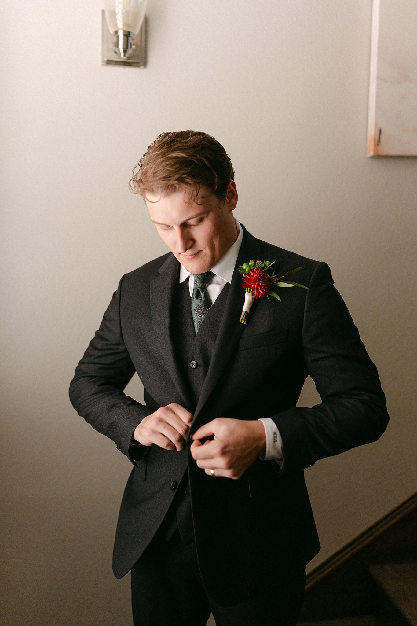 A groom buttons hist suit jacket in a hallway while getting ready at The Brooks At Weatherford