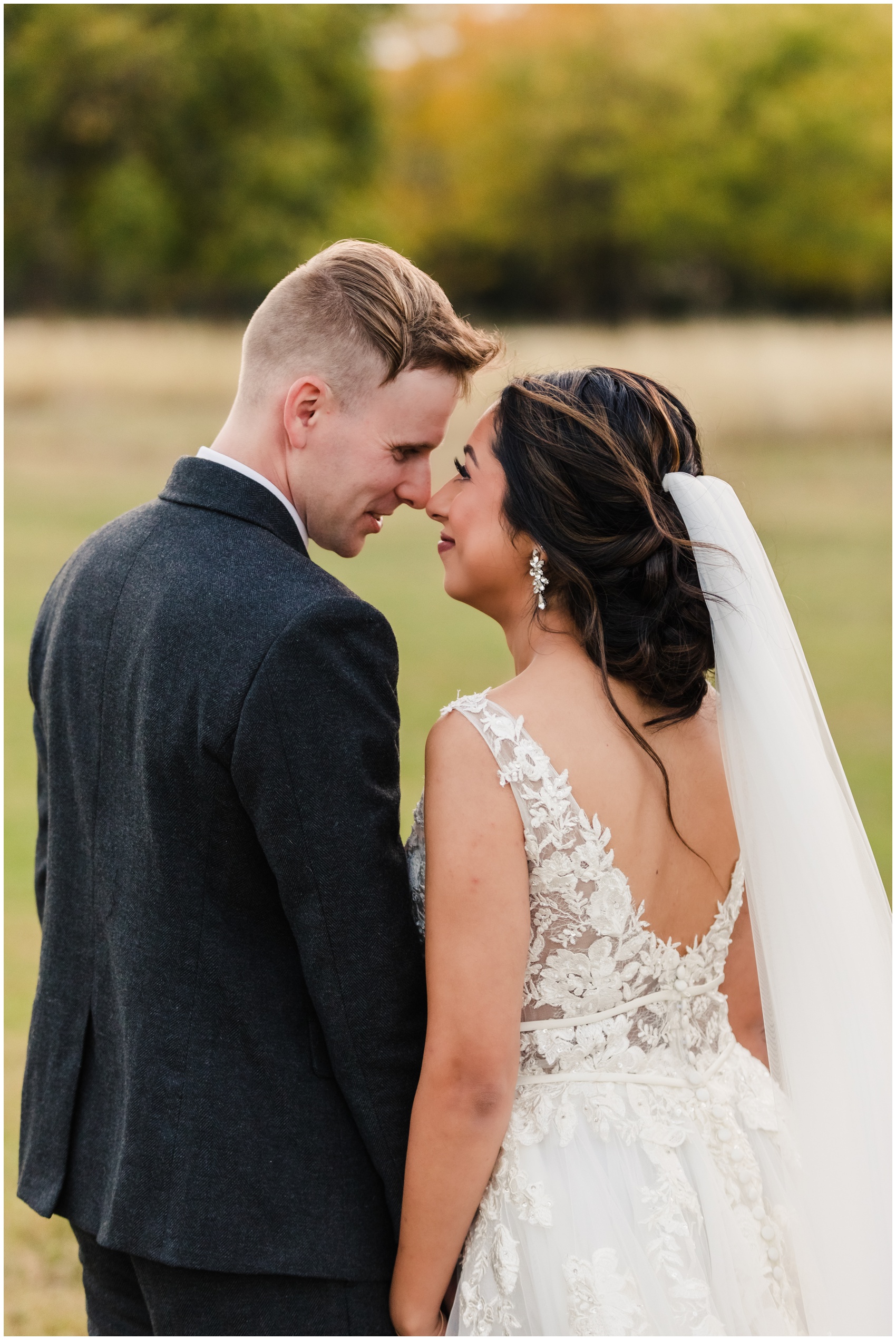 Newlyweds touch noses while holding hands in a field at sunset