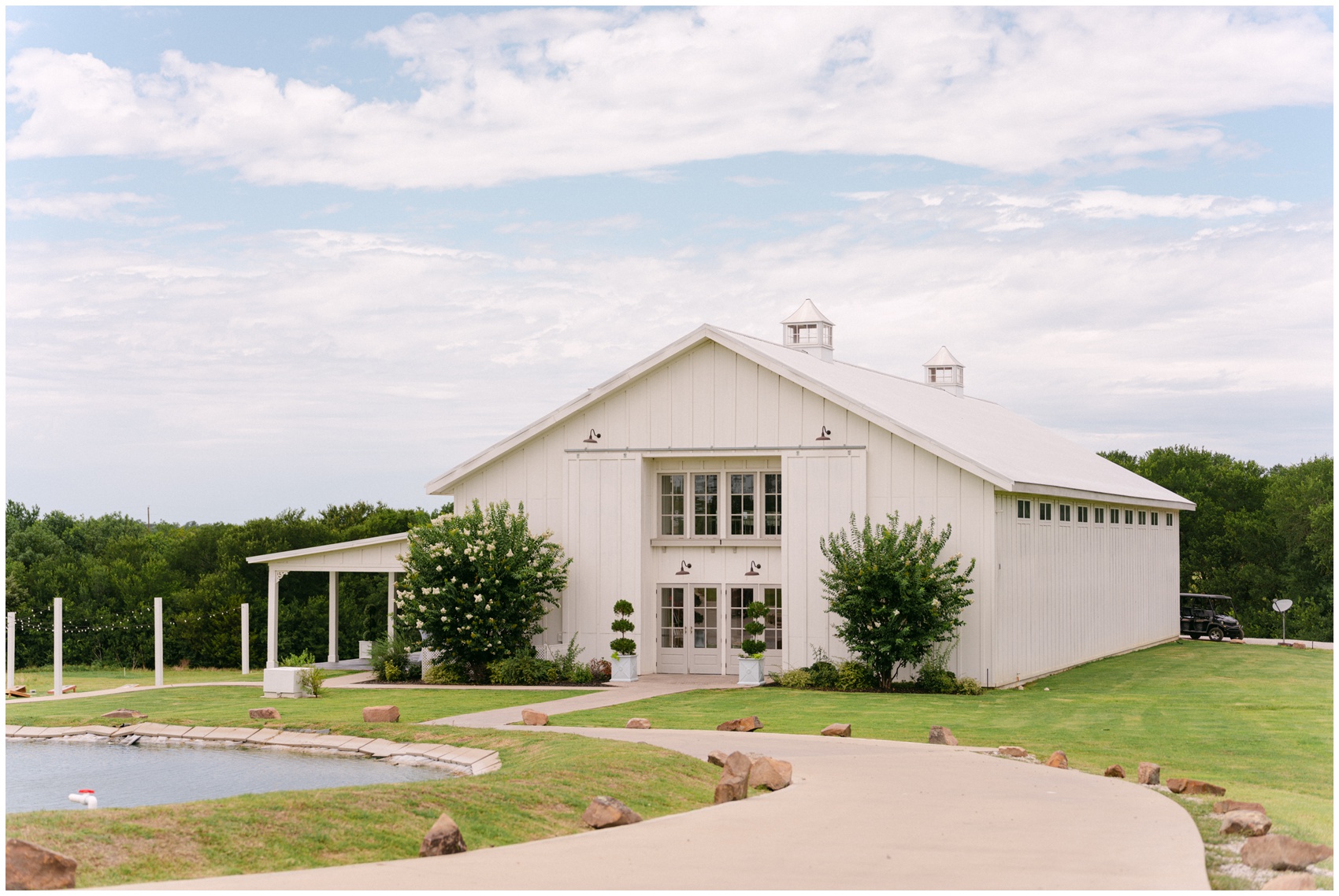 A view of the front entrance of a white barn wedding venue by a lake