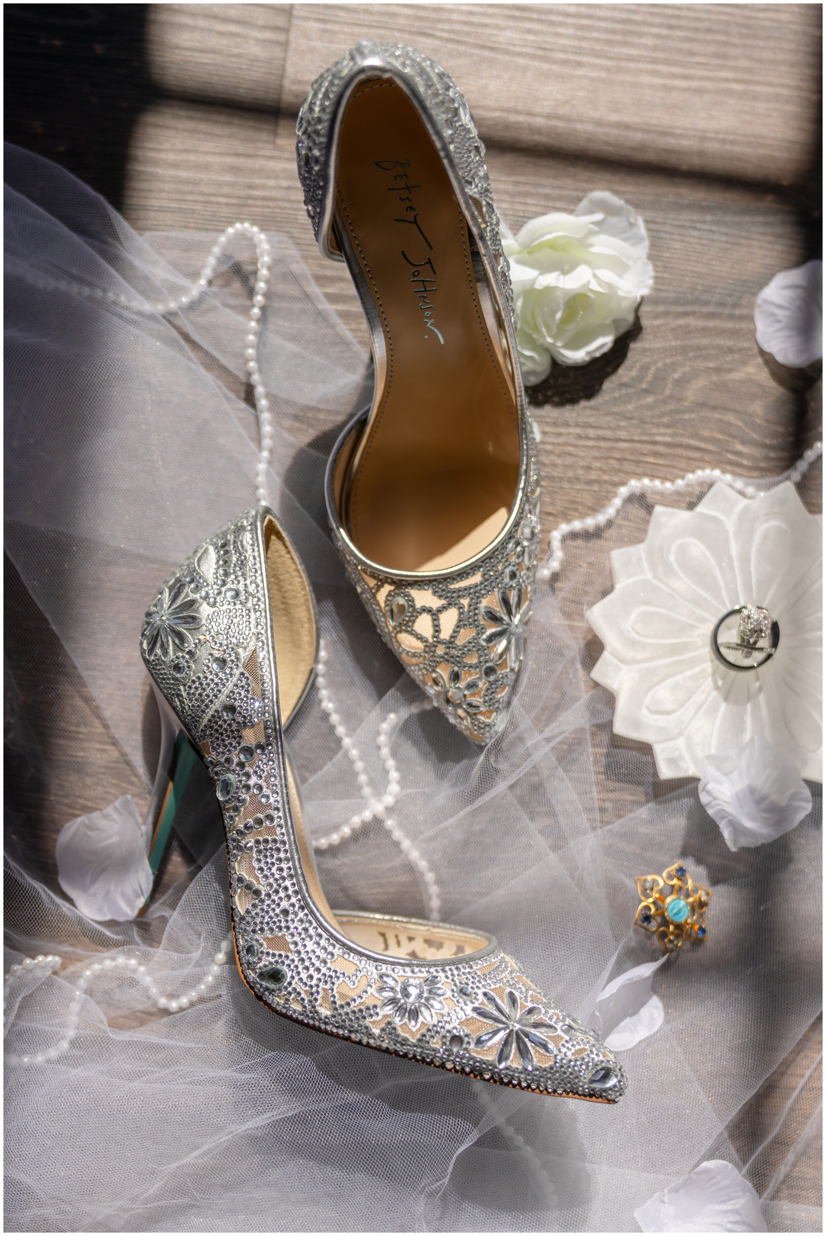 Details of ornate silver bridal shoes sitting on the floor with the veil and jewelry