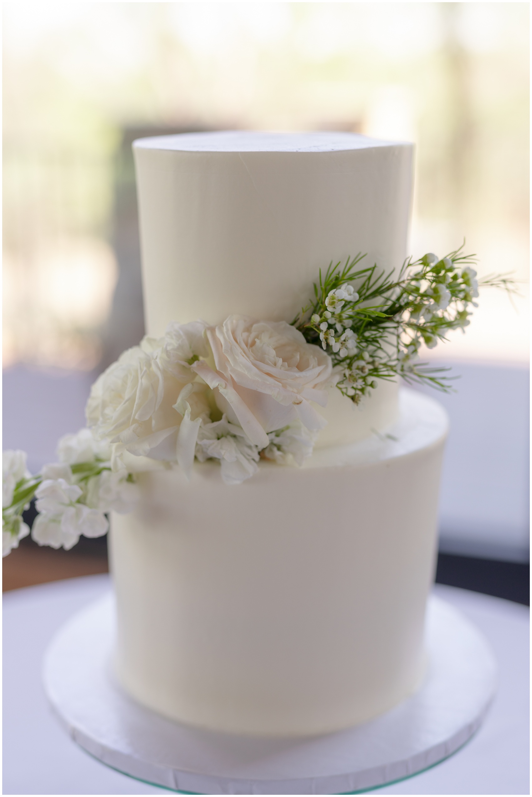 Details of a white cake with white roses on a table un a window at The Mason Dallas Wedding Venue