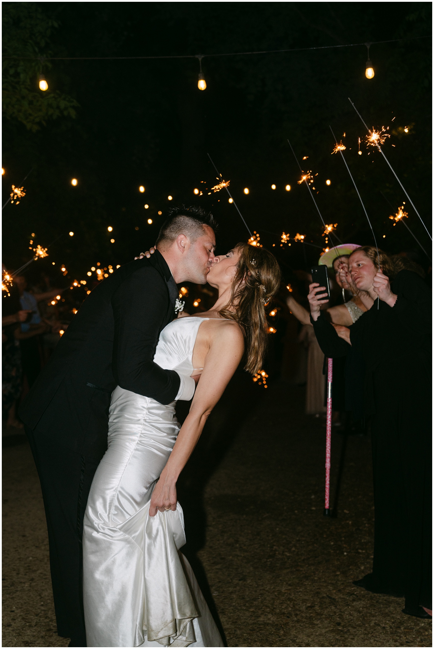 A bride and groom kiss and dip under sparklers and market lights